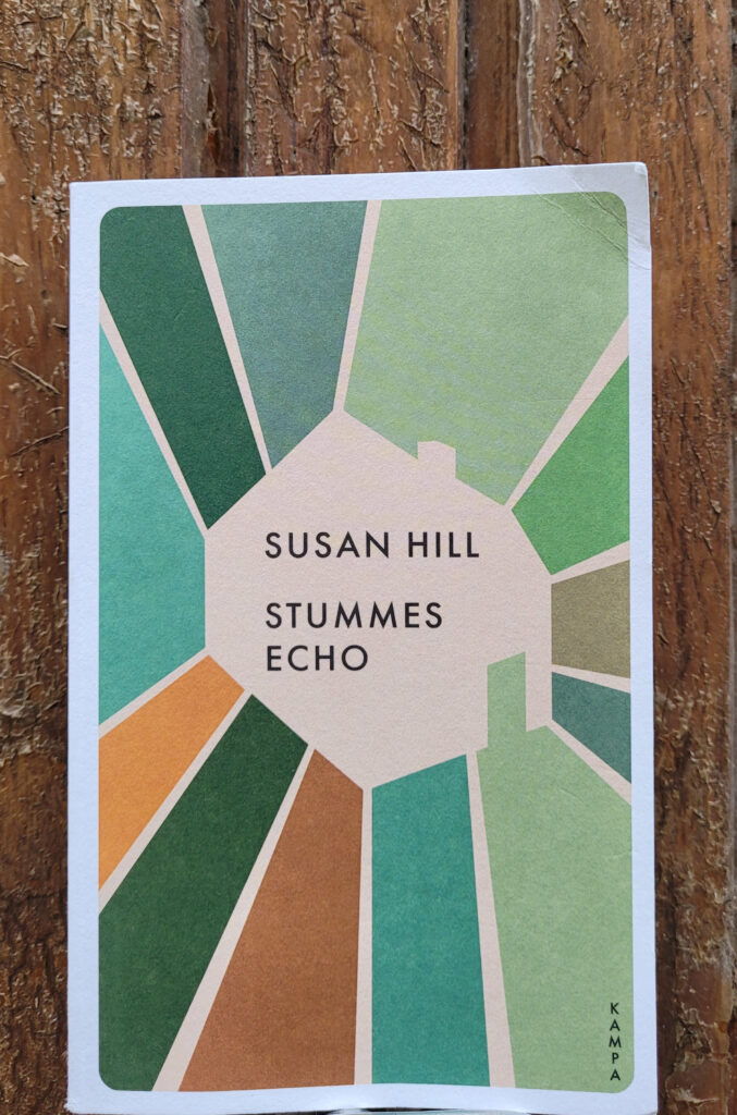 Der Roman „Stummes Echo“ von Susan Hill vor einer verwitterten Holzwand