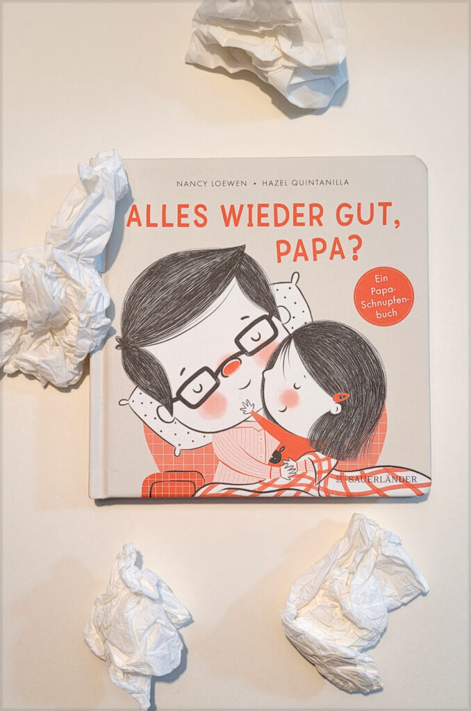 Das Bilderbuch „Alles wieder gut, Papa?“ von Nancy Loewen und Hazel Quintanilla umgeben von verknautschten Taschentüchern