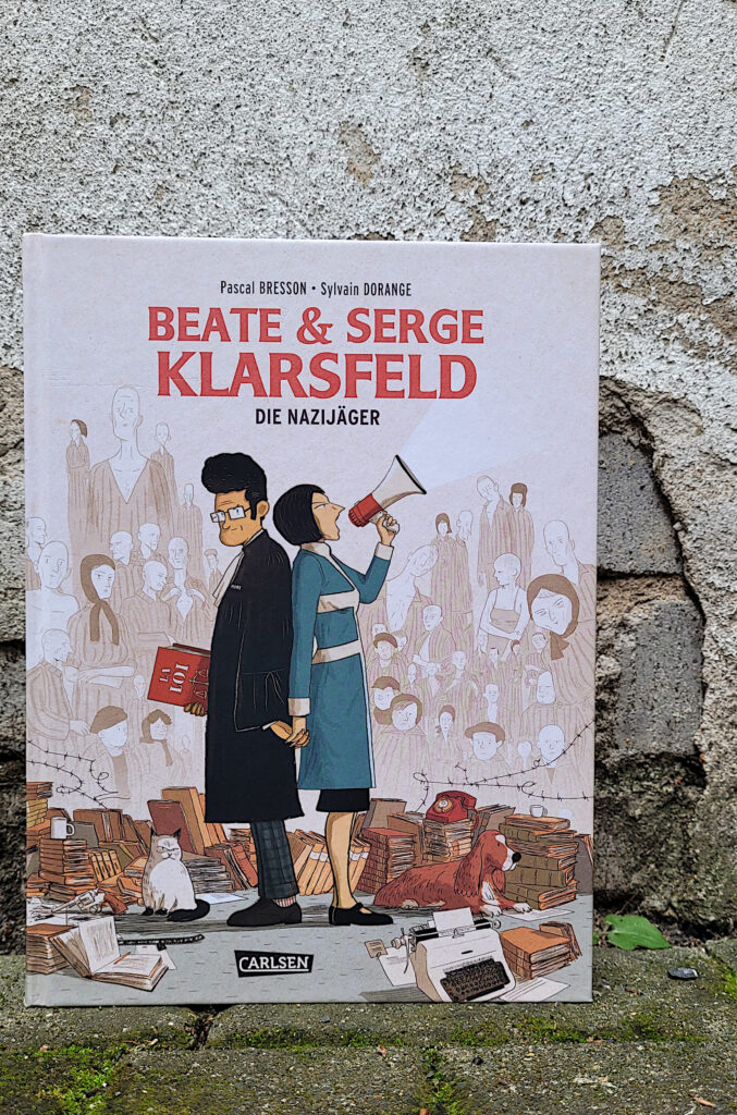 Das Comic-Buch: „Beate und Serge Klarsfeld: Die Nazijäger“ von Pascal Bresson und Sylvain Dorange vor einer kaputten Mauer