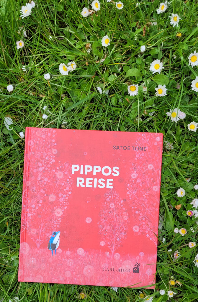 Bilderbuch „Pippos Reise“ von Satoe Tone auf einer Frühlingswiese voller Gänseblümchen