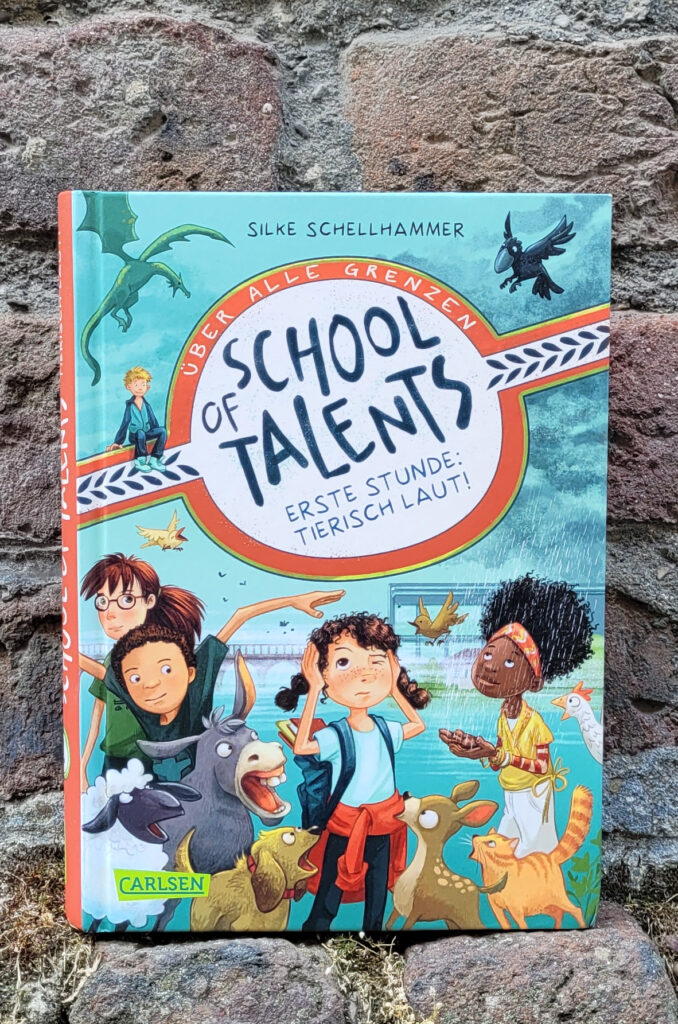 Das Kinderbuch „School of Talents 1 - Erste Stunde: Tierisch laut!“ von Silke Schellhammer vor einer alten Backsteinmauer