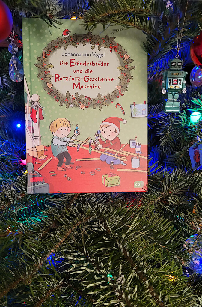 Das Adventskalenderbuch „Die Erfinderbrüder und die Ratzfatz-Geschenke-Maschine“ von Johanna von Vogel in einem geschmückten Weihnachtsbaum
