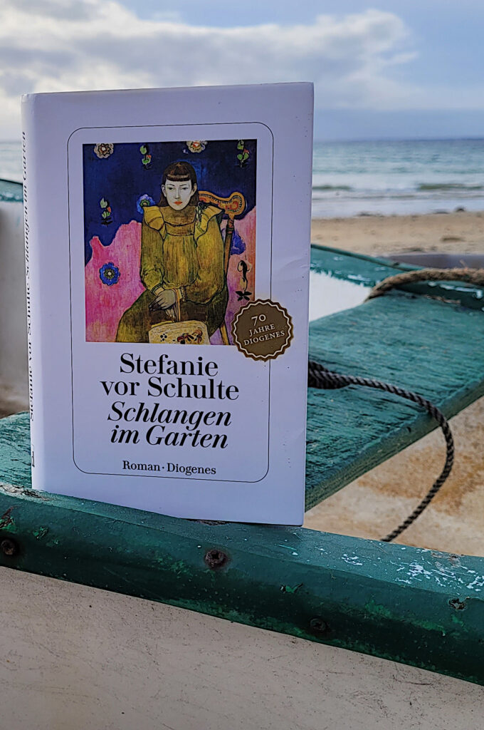 Der Roman „Schlangen im Garten“ von Stefanie vor Schulte in einem Boot am Meer