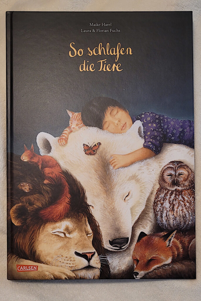 Das Bilderbuch „So schlafen die Tiere“ von Maike Harel sowie Laura und Florian Fuchs auf einer hellen Kuscheldecke liegend.