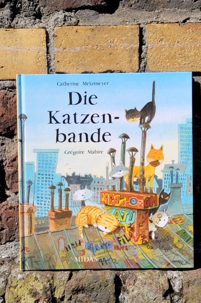 Das Bilderbuch „Die Katzenbande“ von Catherine Metzmeyer und Grégoire Mabire vor einer Backsteinmauer