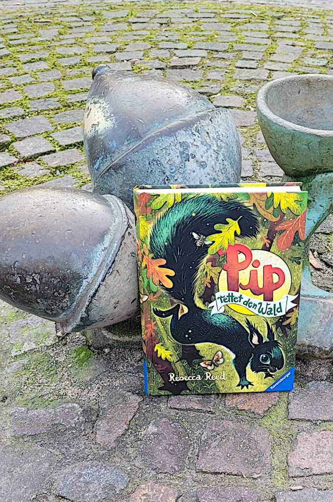 Das Kinderbuch „Pip rettet den Wald“ von Rebecca Reed vorm Eichel-Brunnen An der Eiche in Köln