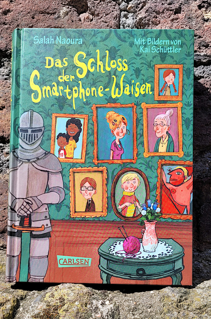 Das Kinderbuch „Das Schloss der Smartphone-Waisen“ von Salah Naoura vor einer verblassten, roten Backsteinmauer