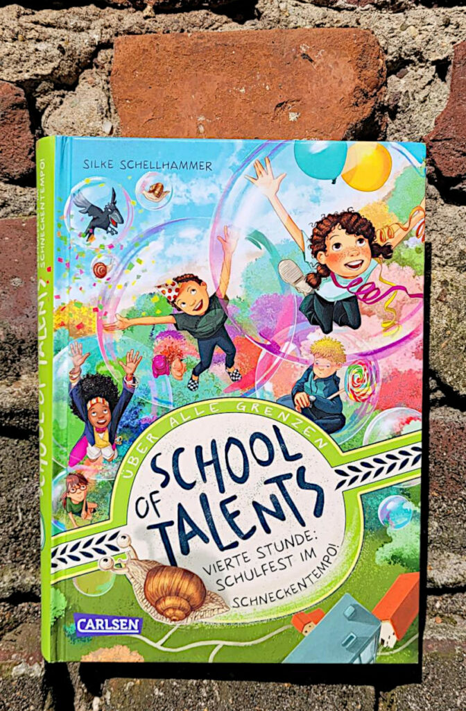 Das Kinderbuch „School of Talents 4: Vierte Stunde – Schulfest im Schneckentempo!“ von Silke Schellhammer vor einer alten Backsteinmauer