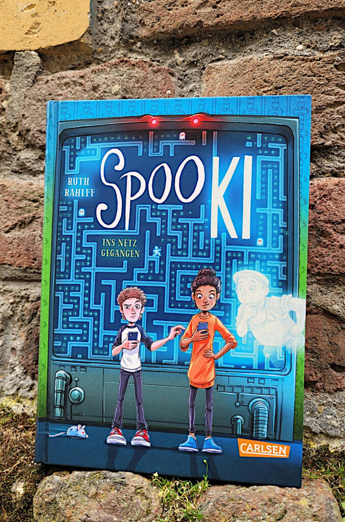 Der Kinder-Sci-Fi-Fantasy-Roman „SpooKI: Ins Netz gegangen“ von Ruth Rahlff vor einer alten Backsteinmauer