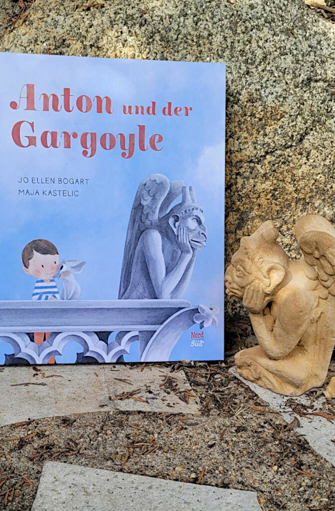 Das Bilderbuch „Anton und der Gargoyle“ von Jo Ellen Bogart und Maja Kastelicvor einem Granitstein mit einem Gargoyle daneben.
