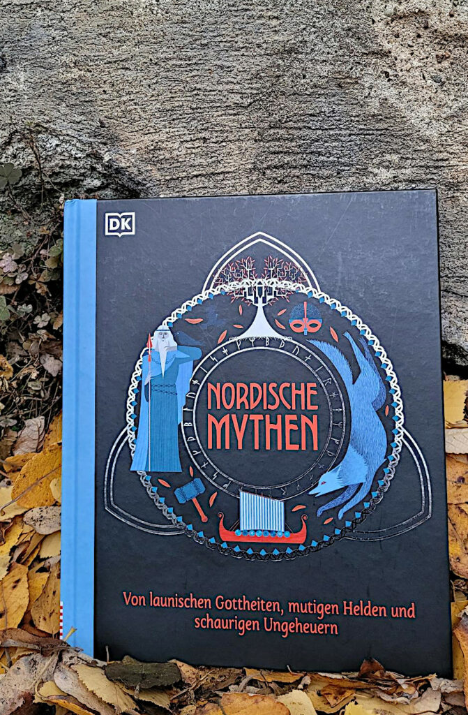 Das Buch „Nordische Mythen“ von Matt Ralphs und Katie Ponder vor einer Mauer in Herbstlaub stehend