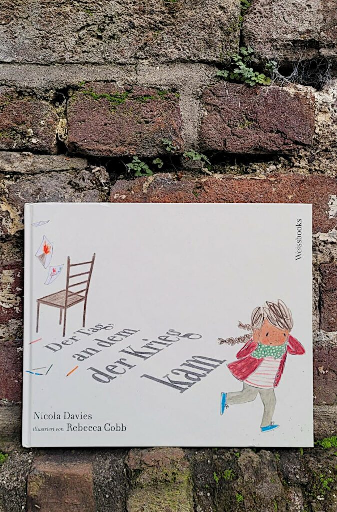 Das Bilderbuch „Der Tag, an dem der Krieg kam“ von Nicola Davies und Rebecca Cobb vor einer roten Backsteinmauer