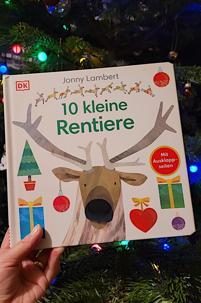 Das Weihnachtsbuch „10 kleine Rentiere“ von Sandra Grimm und Jonny Lambert vor einem Weihnachtsbaum