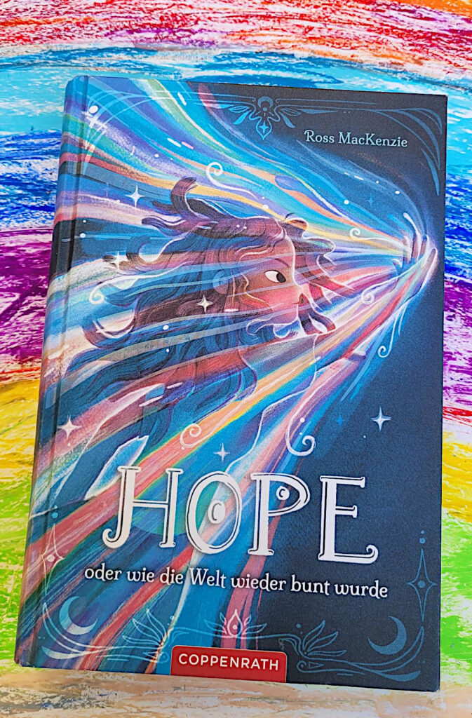 Das BBuch „Hope - oder wie die Welt wieder bunt wurde“ von Ross MacKenzie vor einem mit Wachsmalstiften gemalten Regenbogen