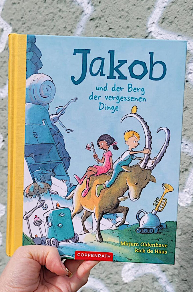 Das Kinderbuch „Jakob und der Berg der vergessenen Dinge“ vor eine grauen Hauswand mit weißen Graffity-Linien