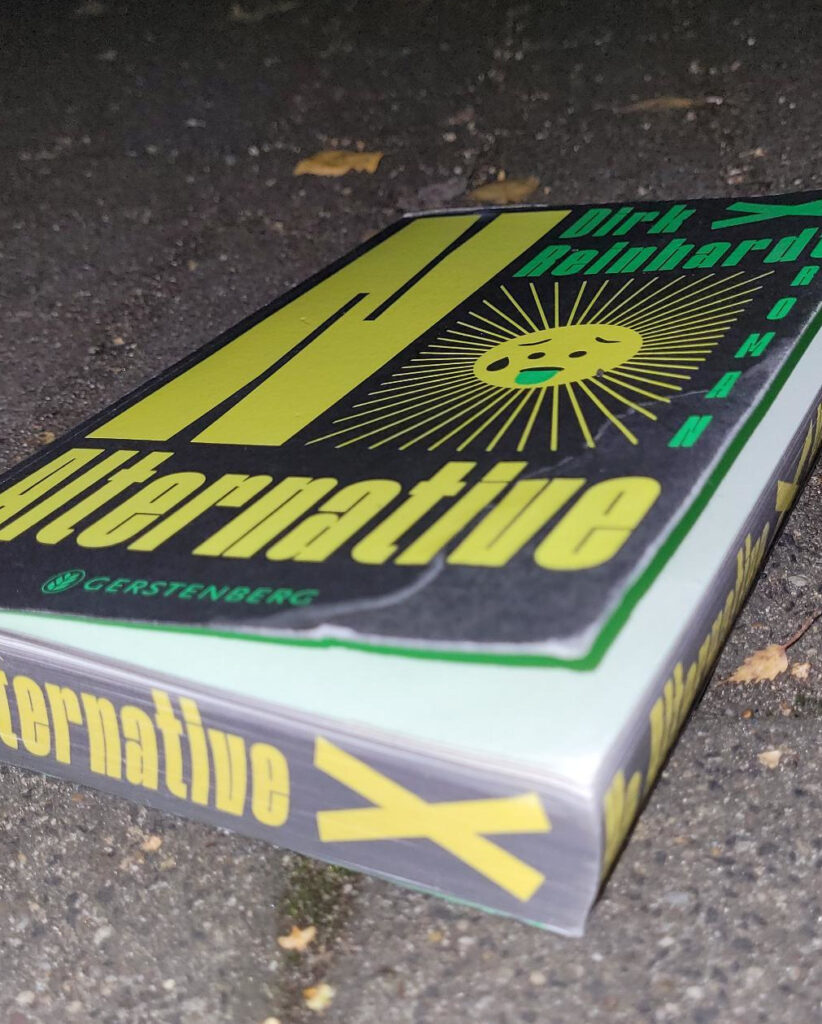 Das Jugendbuch „No Alternative“ von Dirk Reinhardt liegt auf Betonboden, der Farbschnitt des Buches ist gut sichtbar
