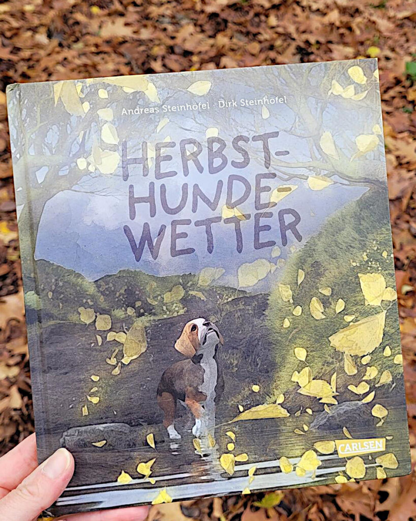 Das Bilderbuch „Herbsthundewetter“ von Andreas und Dirk Steinhöfel vor rotbraunem Herbstlaub