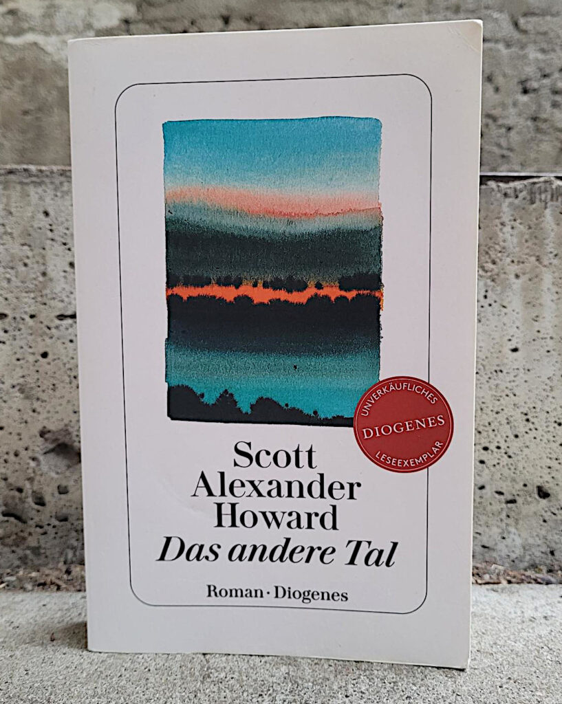 Das unverkäufliche Taschenbuch-Leseexemplar des Romans „Das andere Tal“ von Scott Alexander Howard vor eine brüchigen, grauen Betonwand.